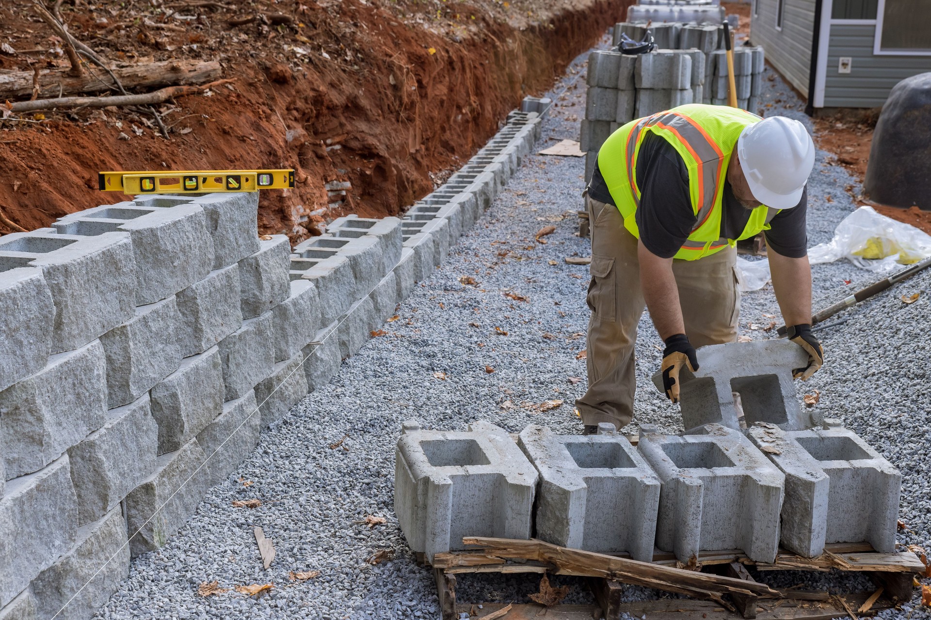 Construction site worker installing the newly constructed large block retaining wall as part of the construction of a new building